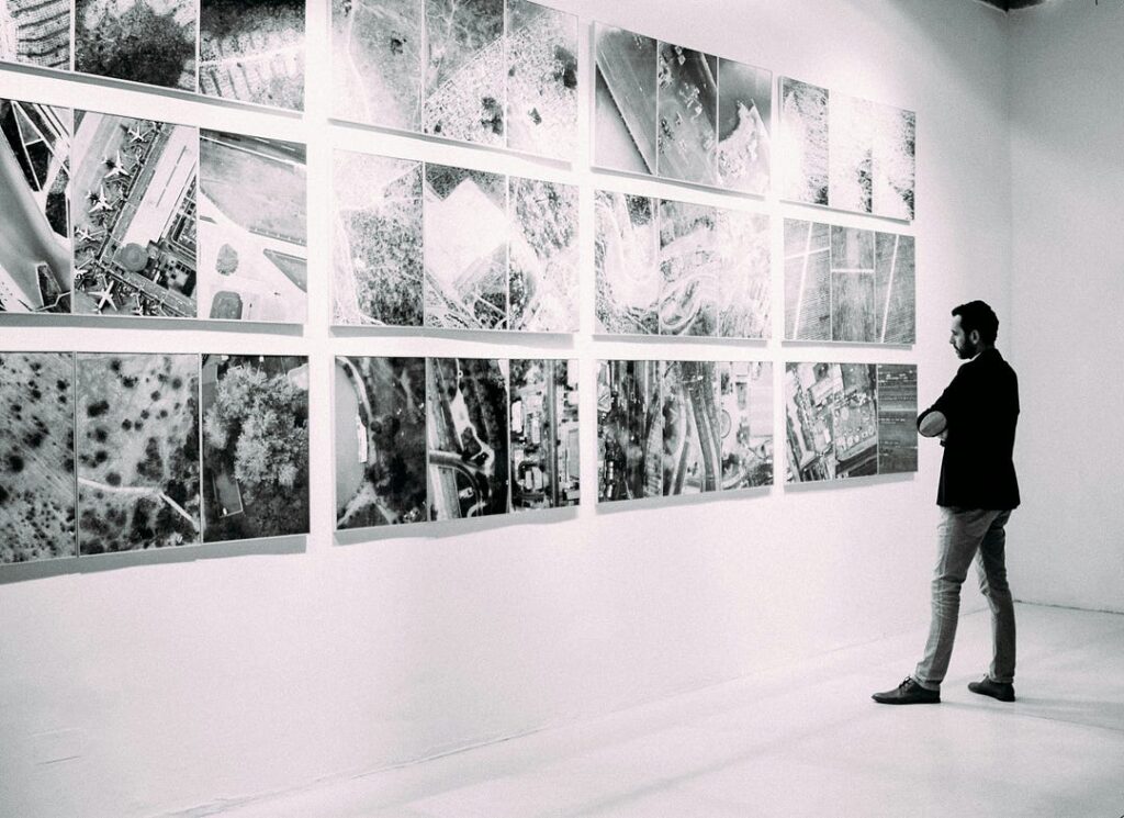 Black and white photo of a person standing, looking at a wall of art